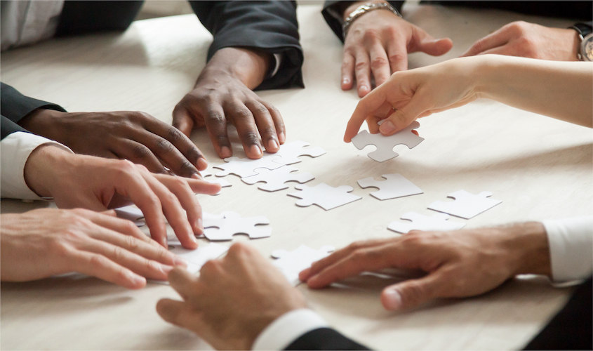 Hands of a diverse group of people completing a puzzle