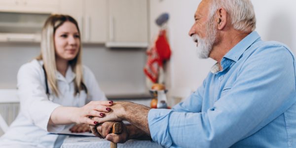 Young positive caregiver taking care of senior man in nursing home