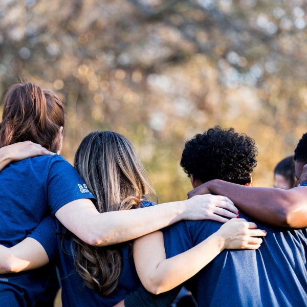 Diverse group of friends cleanup a park during a charity event. They are standing with their arms around one another.